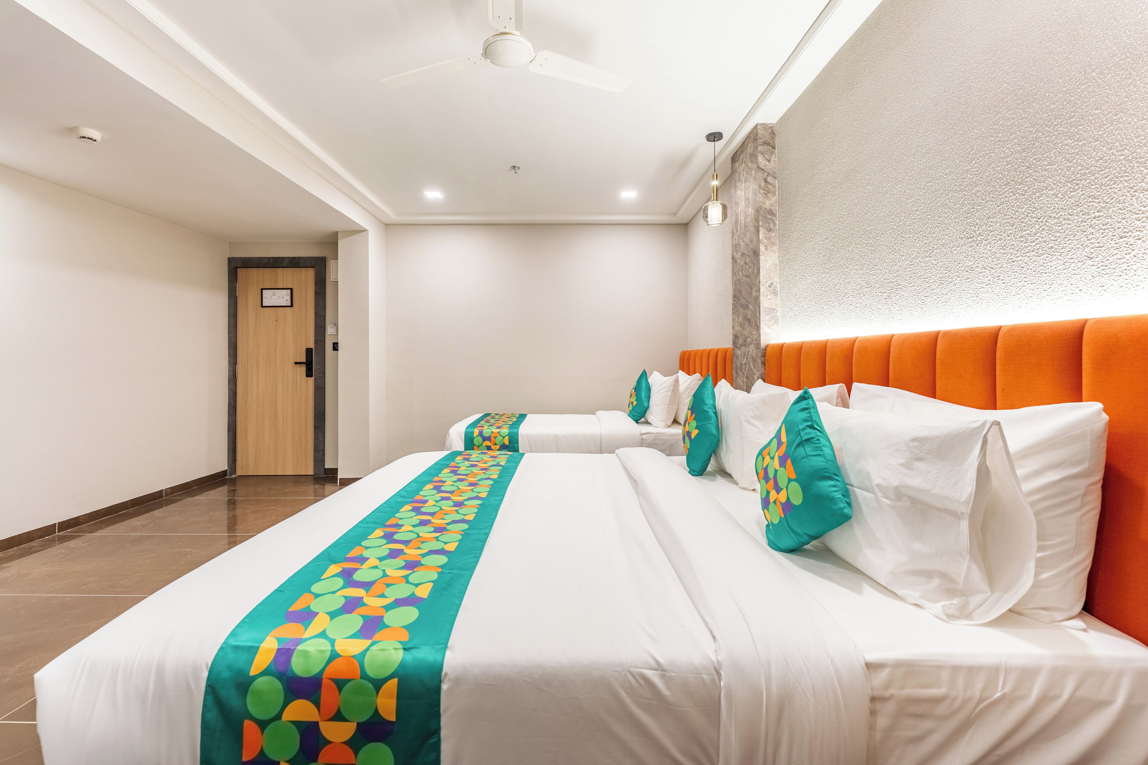 A hotel room with two beds, a ceiling fan, and a door leading to another room.