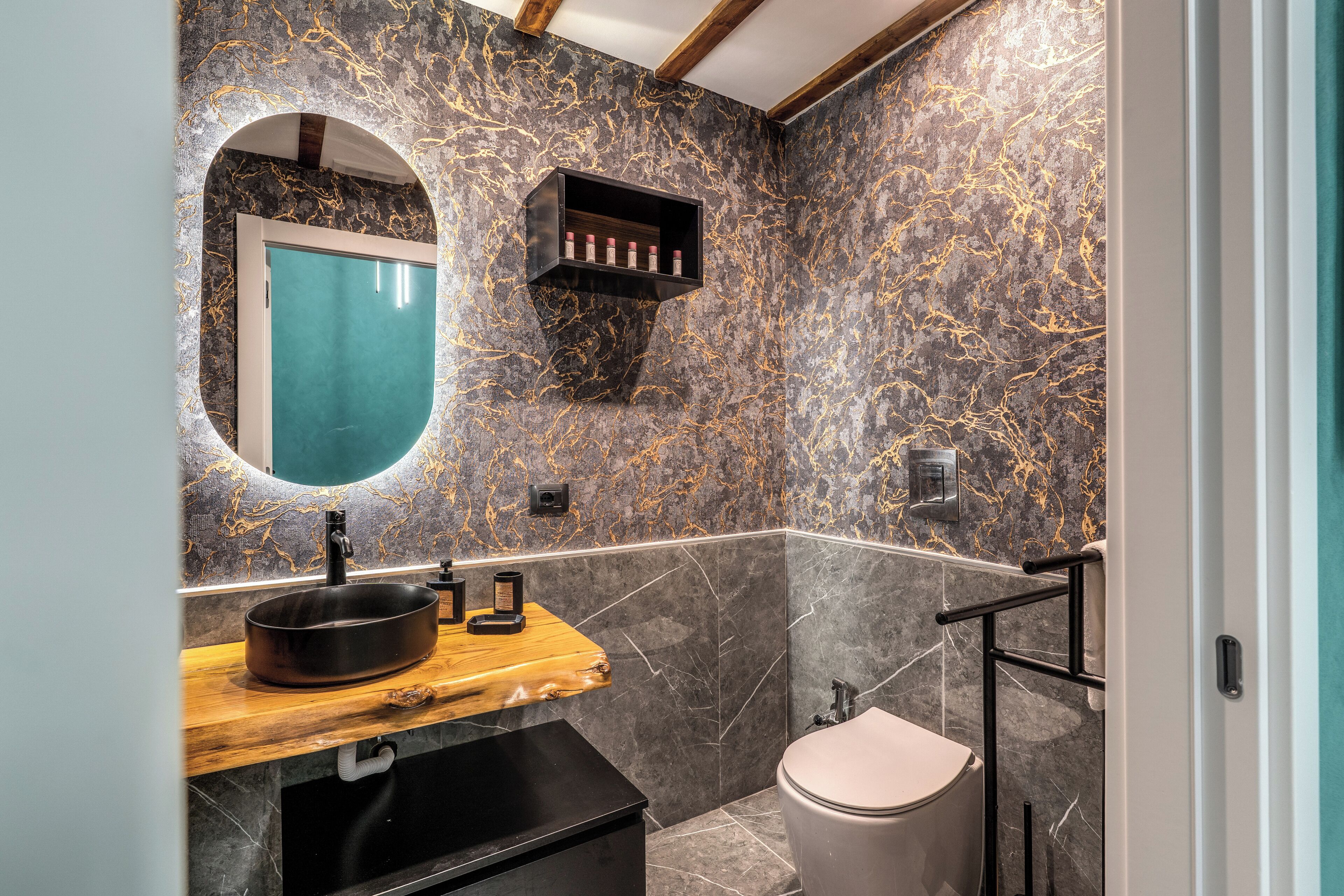A modern bathroom with a marble backsplash, a wooden vanity, a black sink, and a toilet.