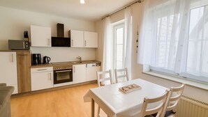 Kompakti keittiö, jossa on mikroaaltouuni, kahvinkeitin, uuni sekä ruokailutila pöydän ja tuolien kera.