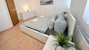 Makuuhuoneessa on sänky, yöpöytä, lipasto, huonekasvi ja seinällä taulu.