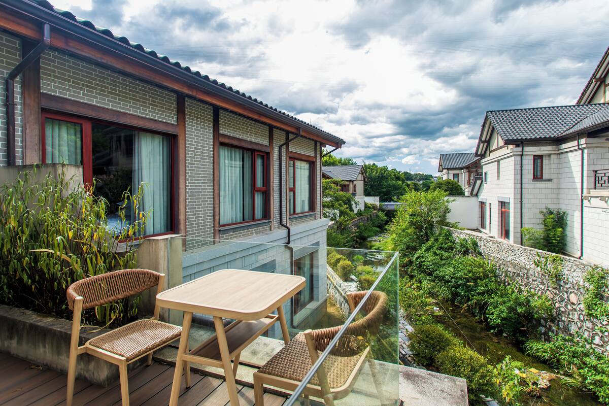 A balcony with a glass railing overlooking a garden and a pond.