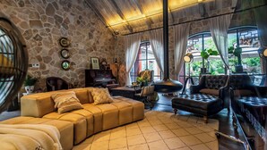 A cozy living room with a stone wall, a wooden ceiling, and a large window with curtains. There is a sofa, a chair, and a piano. - Jingdezhen Homestay Outside the Window (Jingdezhen)
