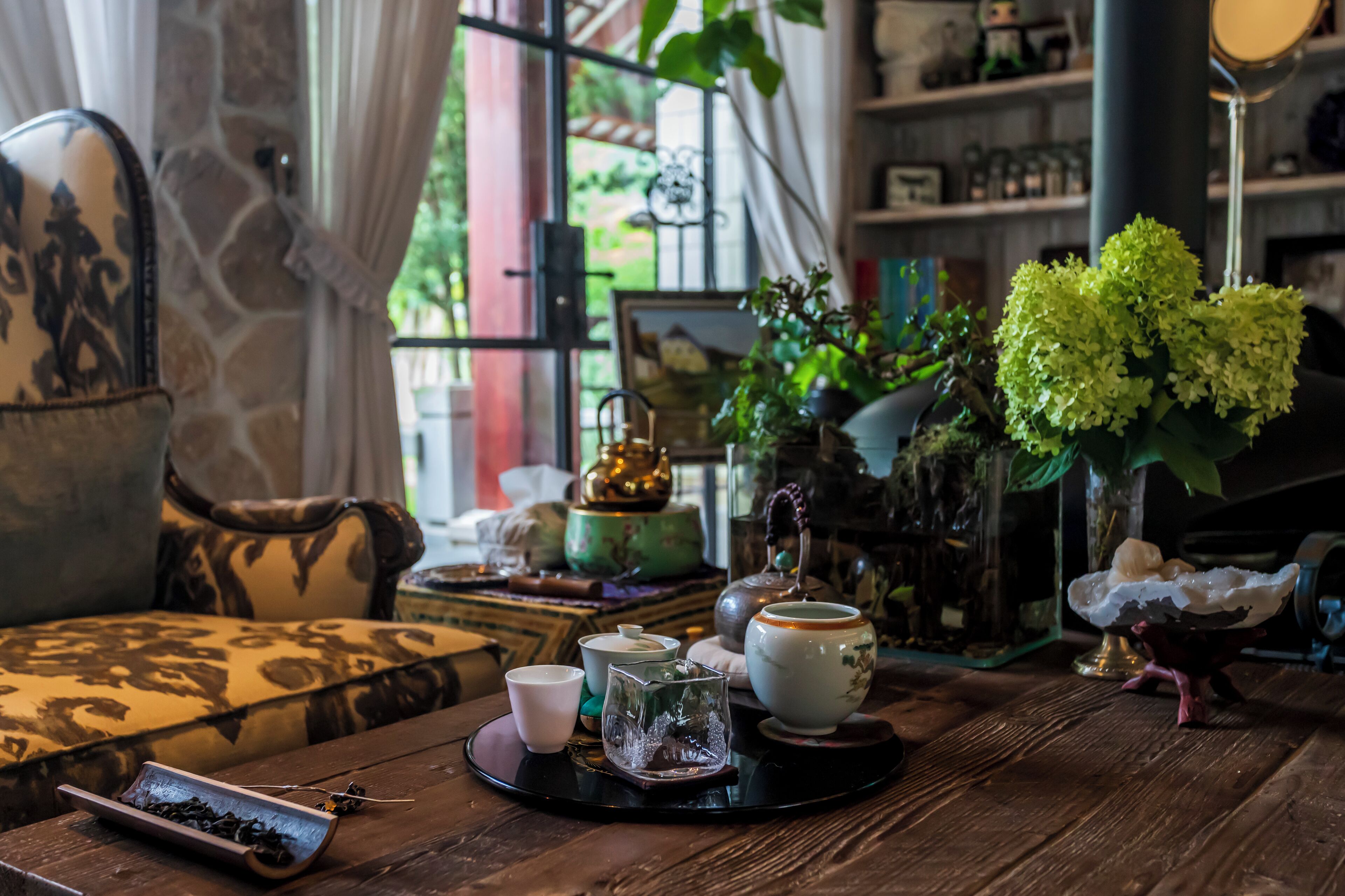 Uma mesa de madeira com um conjunto de chá, um vaso com flores verdes e um espelho decorativo.