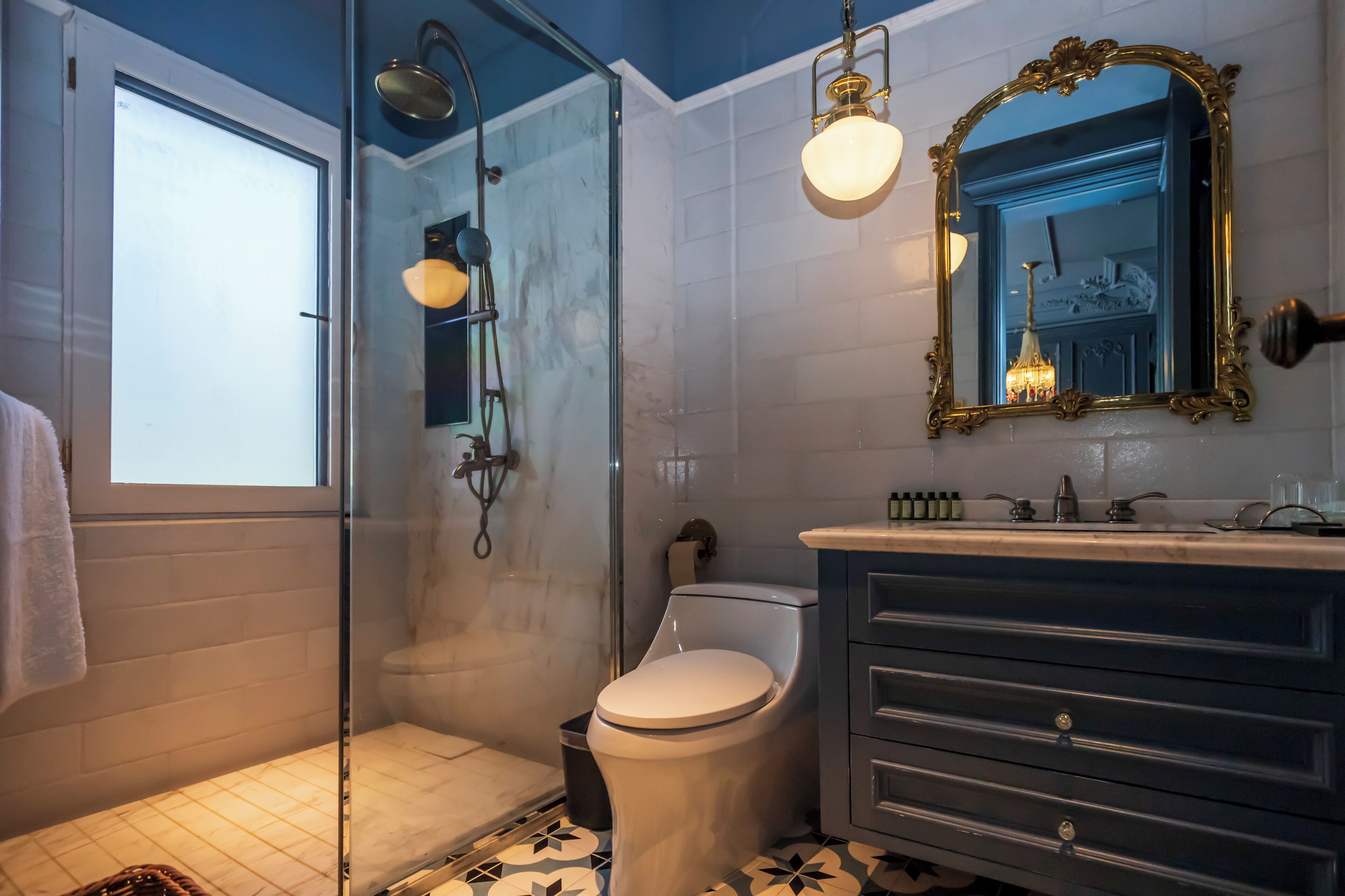 Un baño con cabina de ducha de vidrio, inodoro, tocador con cajones y espejo con marco decorativo.