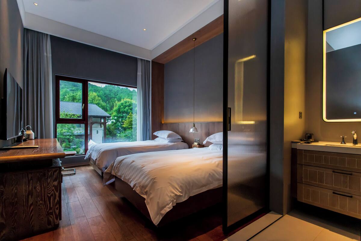 A modern hotel room with a large bed, a desk, and a bathroom with a mirror and sink.