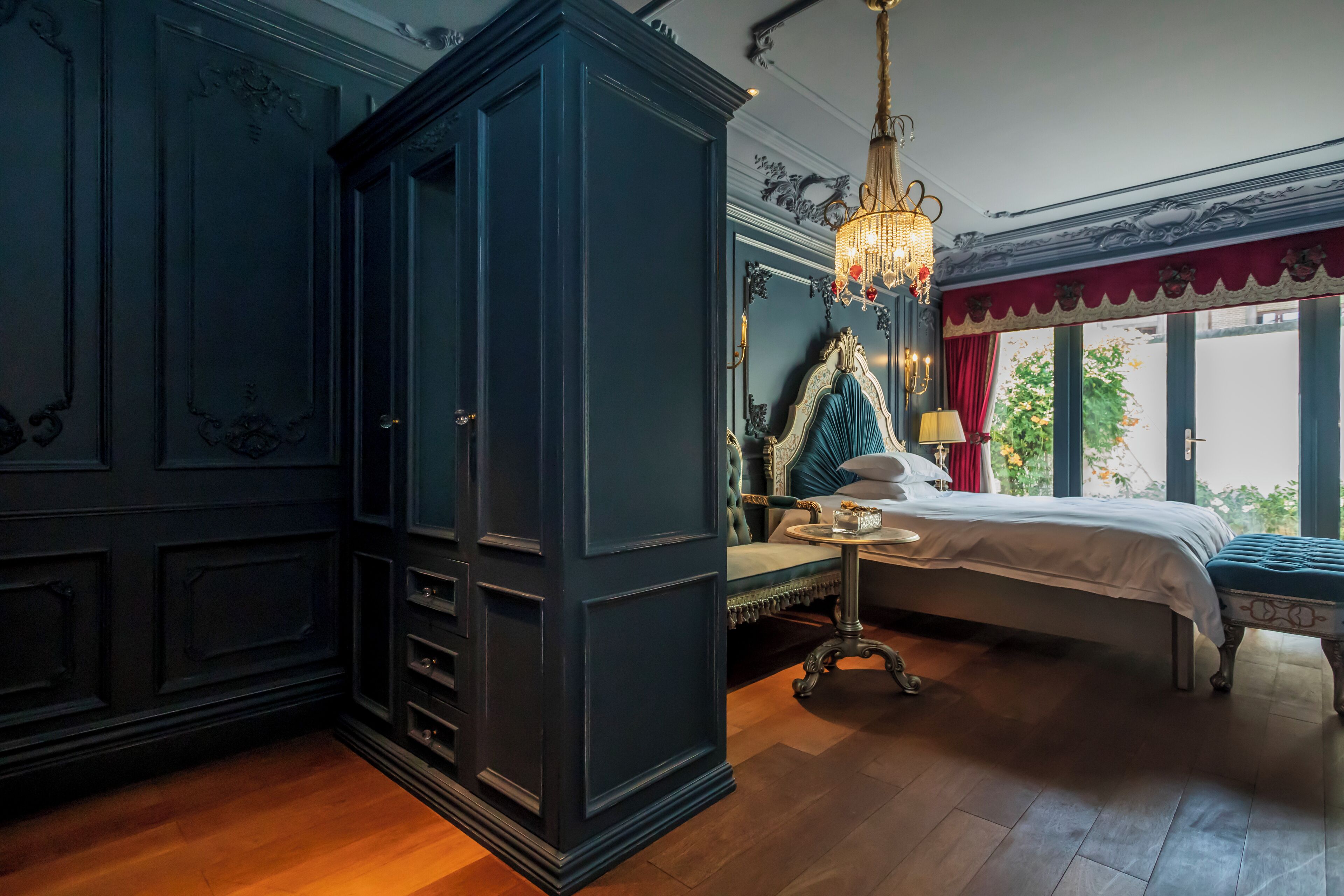 A bedroom with a large dark blue wardrobe, a bed with a white and teal headboard, and a chandelier.