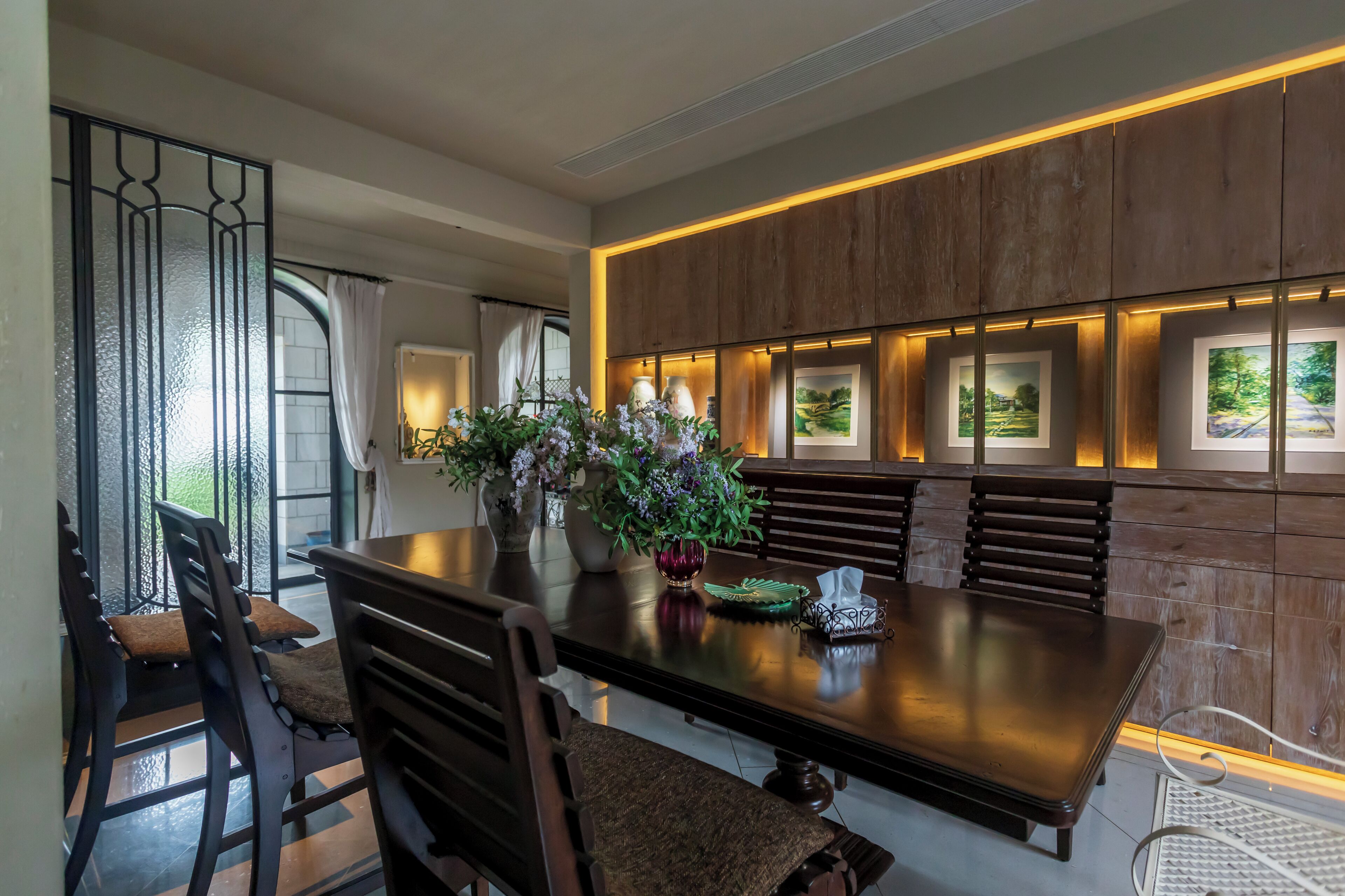 A dining area with a long table, chairs, and a decorative vase with flowers.