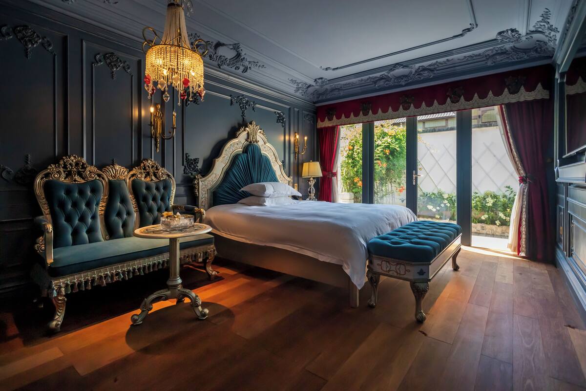 A luxurious bedroom with a large bed, ornate furniture, and a chandelier.