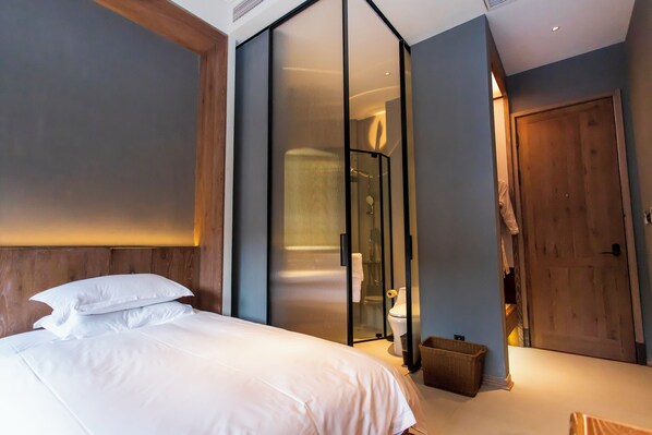 Une chambre d’hôtel moderne avec un grand lit, une douche à parois de verre et une porte en bois.