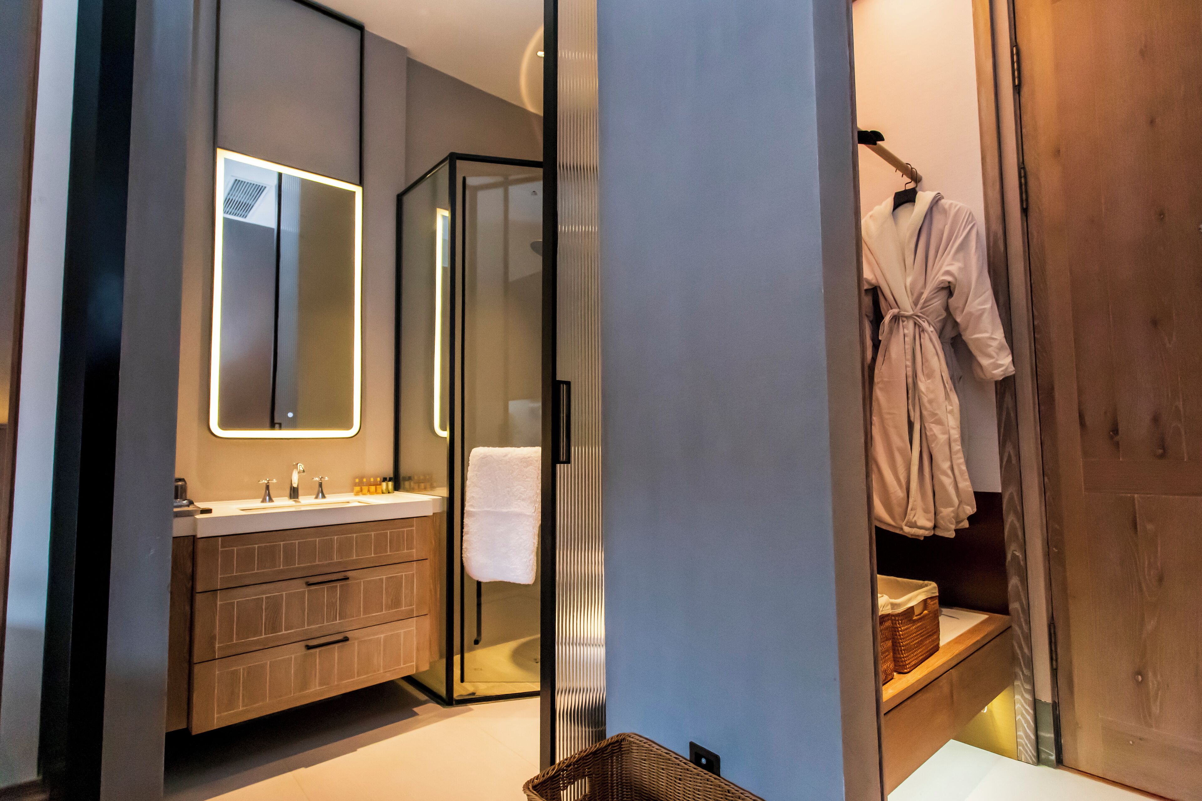 A modern bathroom with a glass shower enclosure, a vanity with a mirror, and a robe hanging on a rack.