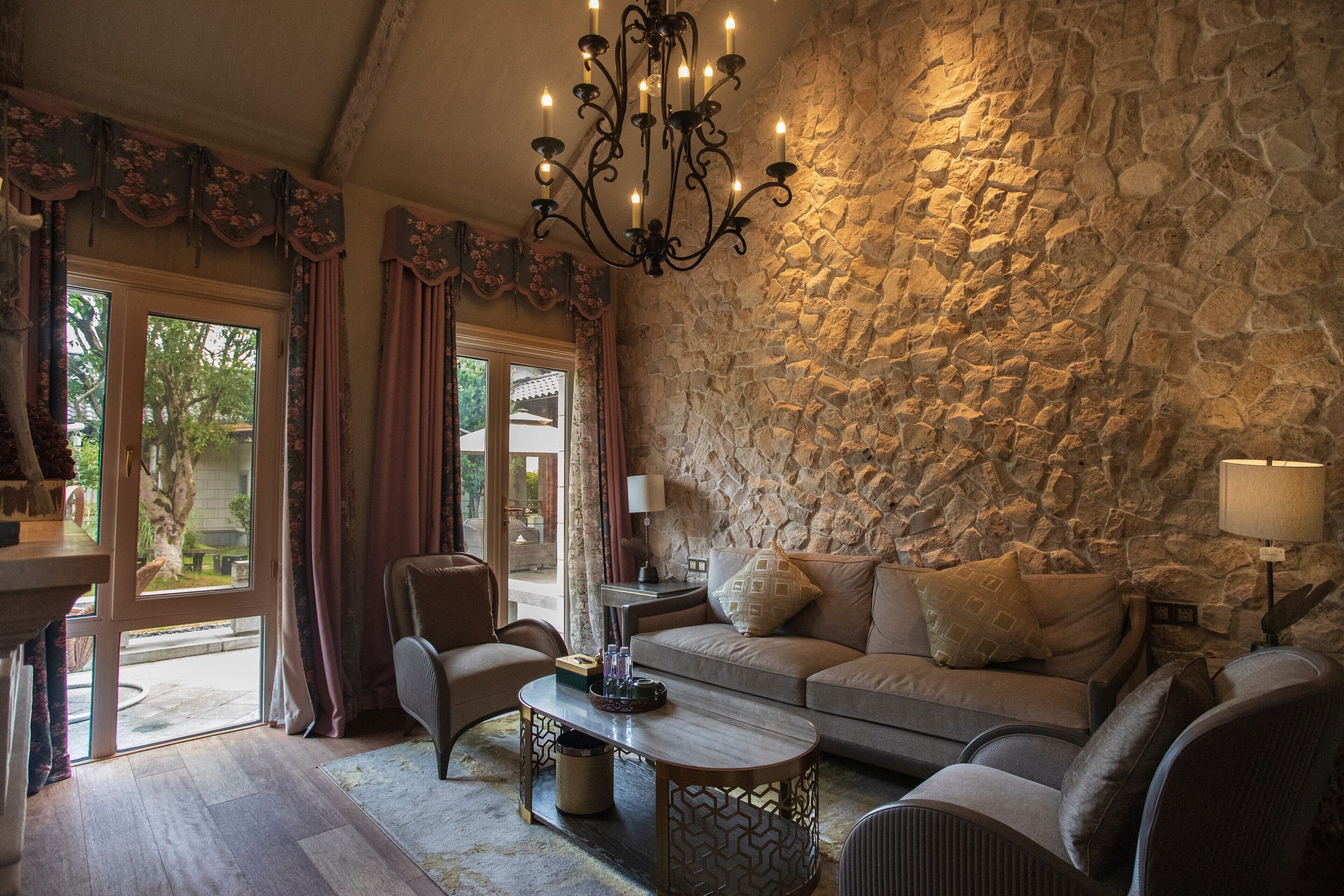 A cozy living room with a stone wall, a chandelier, and a sofa with cushions.