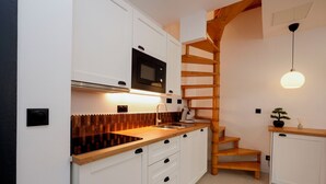 Cozinha com armários brancos, bancada de madeira, micro-ondas embutido e escada de madeira.