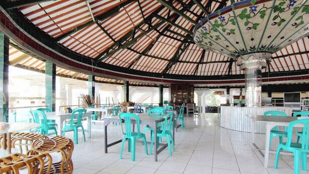 Un vaste espace intérieur aménagé pour les repas, avec de hauts plafonds et une colonne décorative centrale. Des tables et des chaises sont disposées pour accueillir les convives.