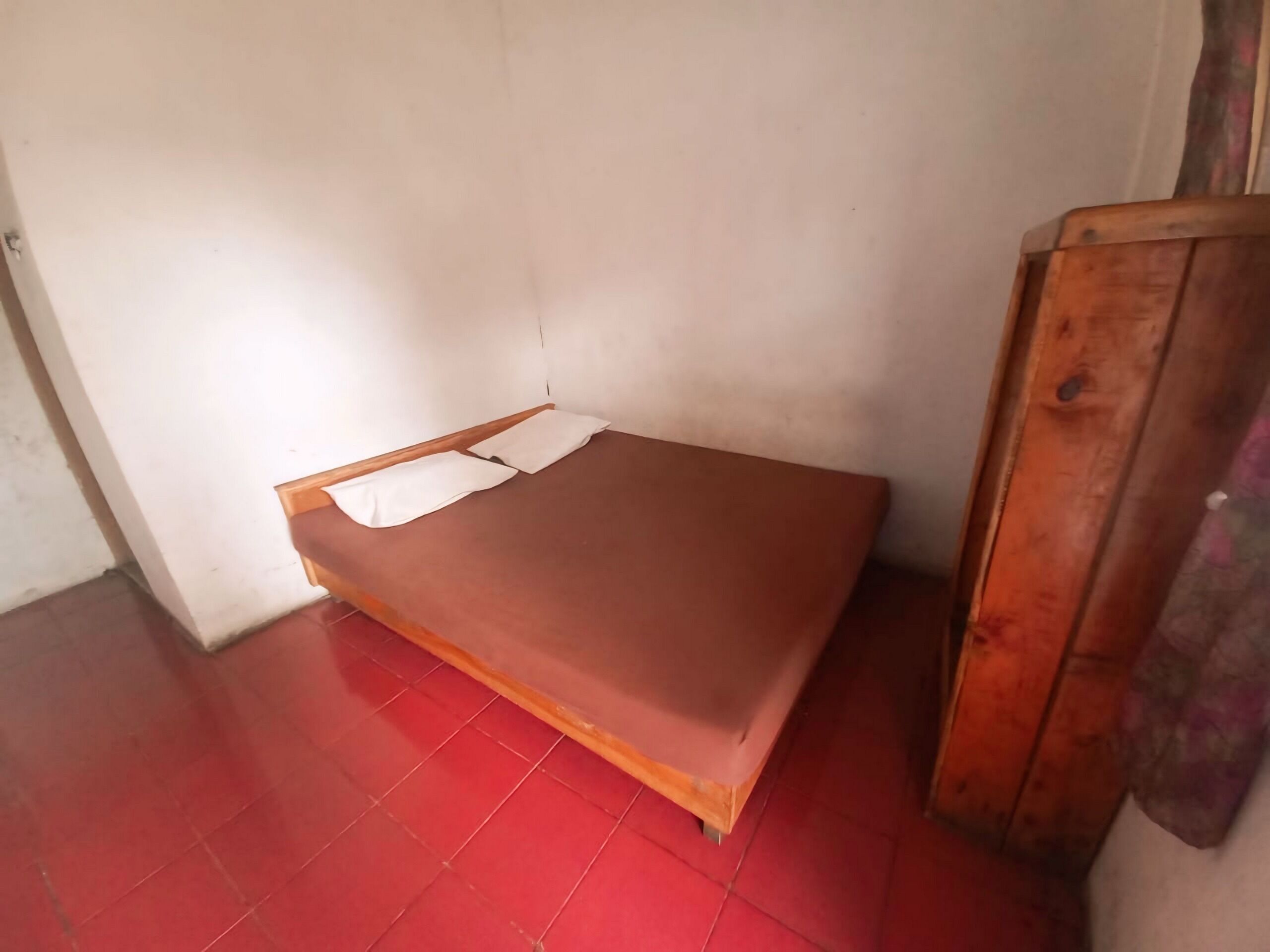 A small, single-bed room with a red-tiled floor and white walls.