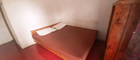 A small, single-bed room with a red-tiled floor and white walls.