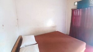 Une petite chambre avec un lit simple, un mur blanc uni et une couverture de lit rouge.