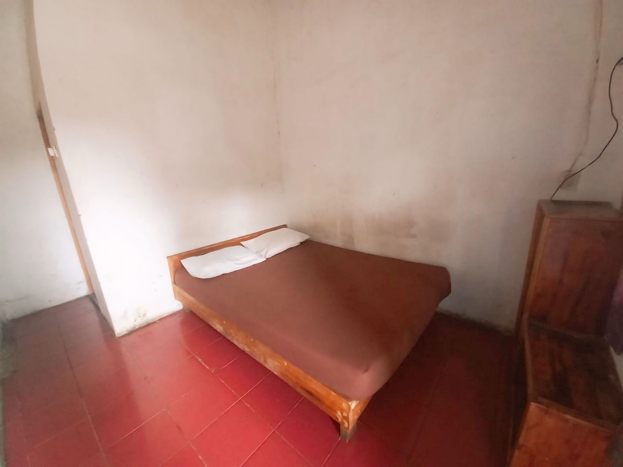 A small, single-bed room with a wooden frame and a red-tiled floor.