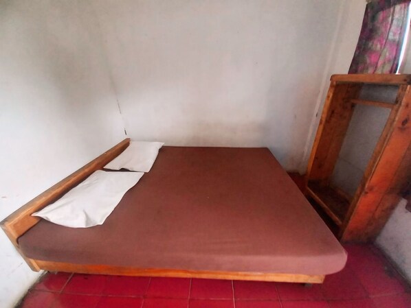 Une petite chambre avec un lit simple, un cadre en bois et un matelas rouge.