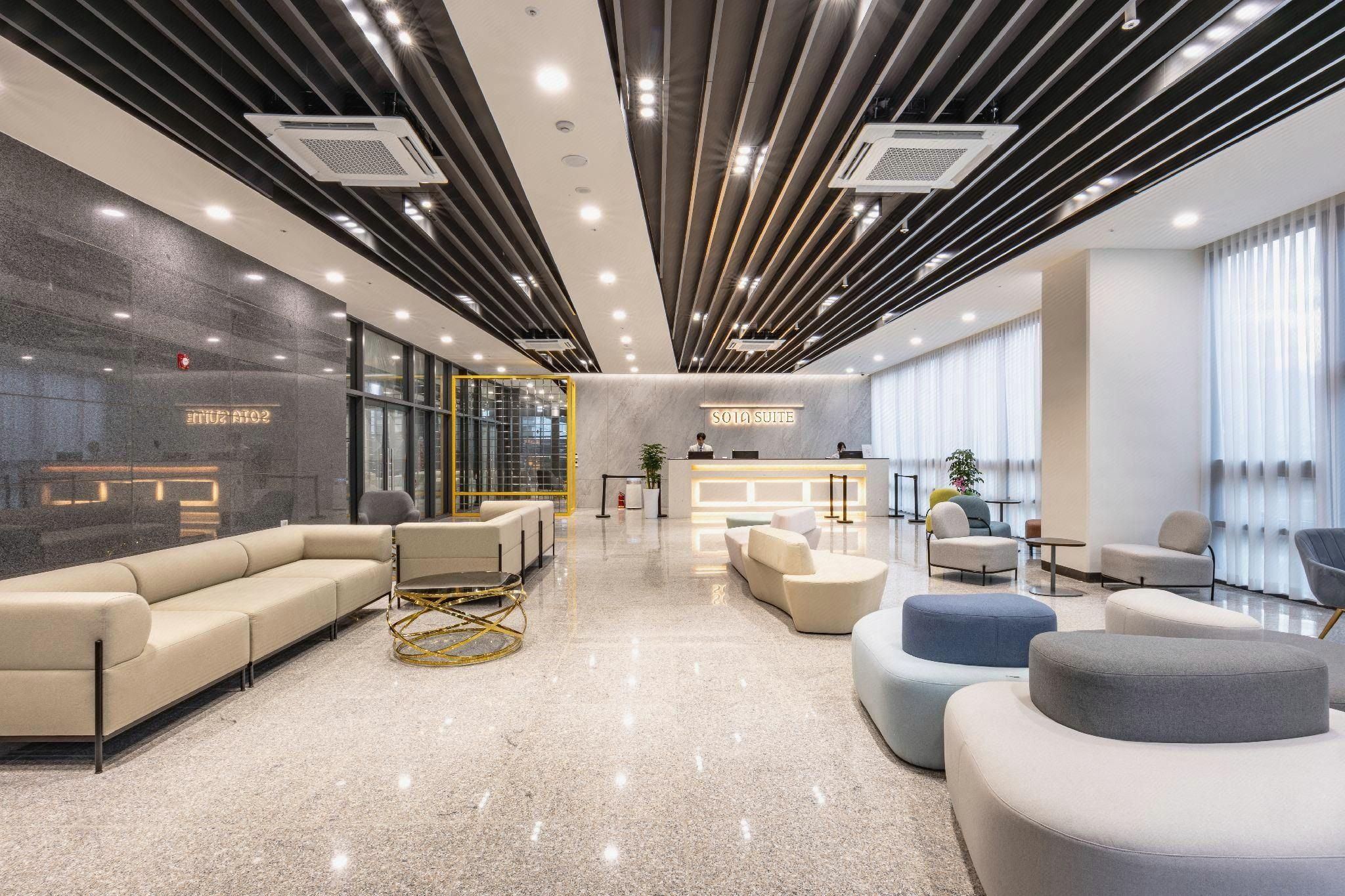 A modern hotel lobby with a reception desk, seating area, and a glass wall.