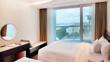 Habitación de hotel con cama, escritorio, espejo y ventana grande con vista a edificios y una masa de agua.