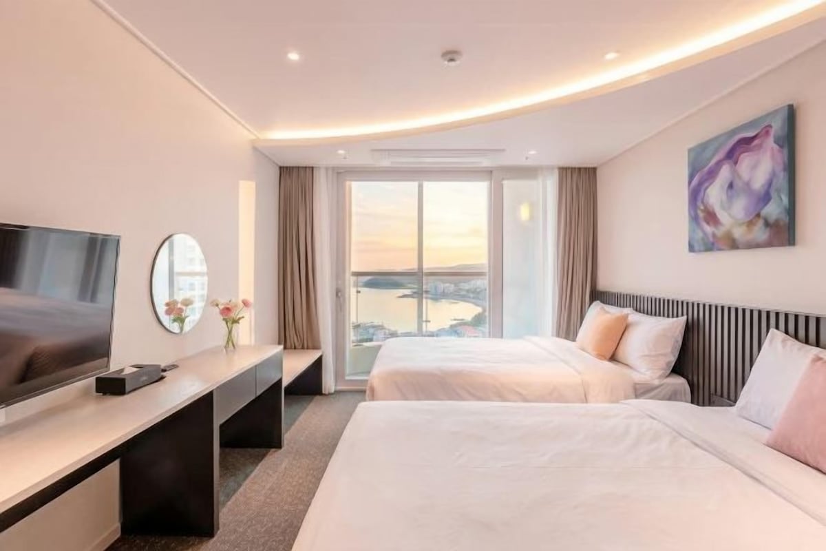 Hotelkamer met twee bedden, een televisie, een bureau en een groot raam met uitzicht.