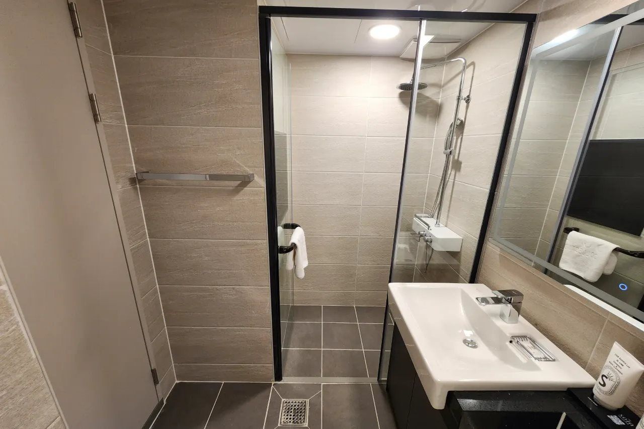 Et moderne badeværelse med en brusekabine i glas, en hvid vask og et spejl der reflekterer interiøret.