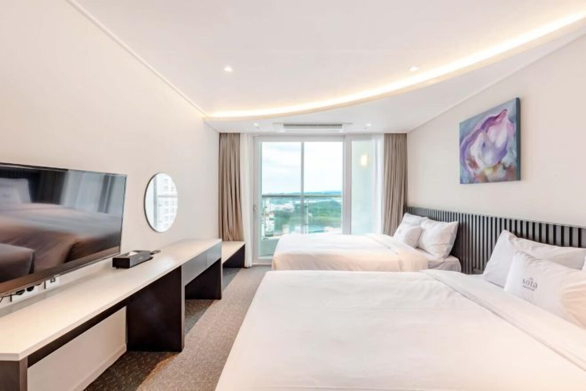 A hotel room with a bed, a TV, a desk, and a window with a view.