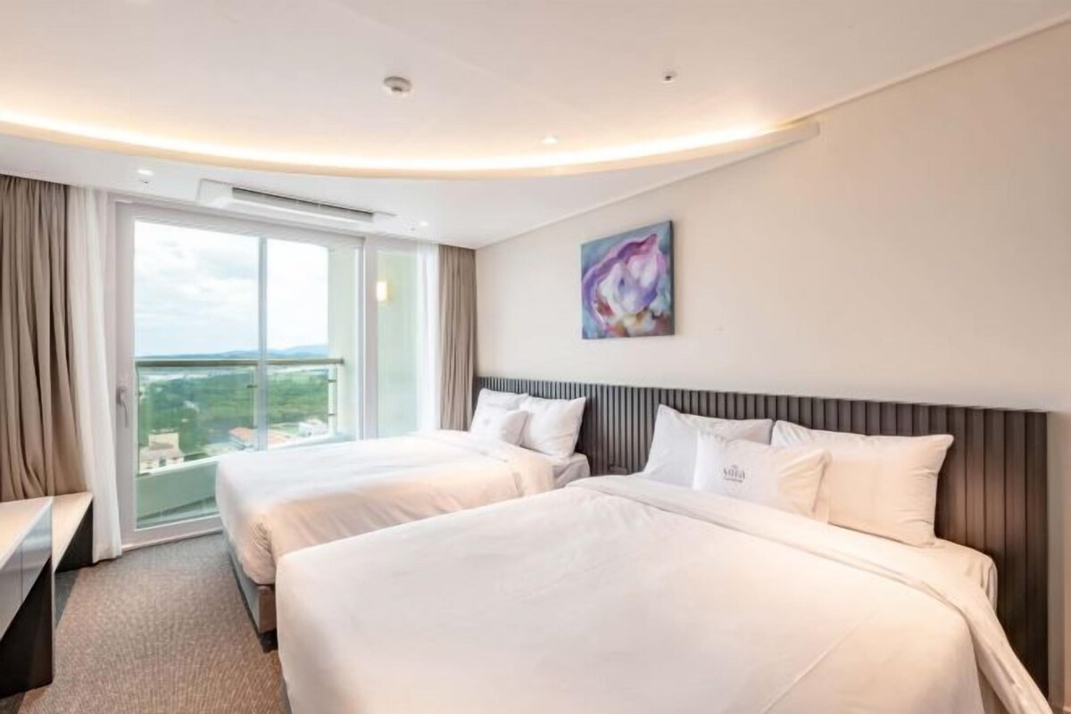 Een hotelkamer met twee bedden, een groot raam met uitzicht en een schilderij aan de muur.