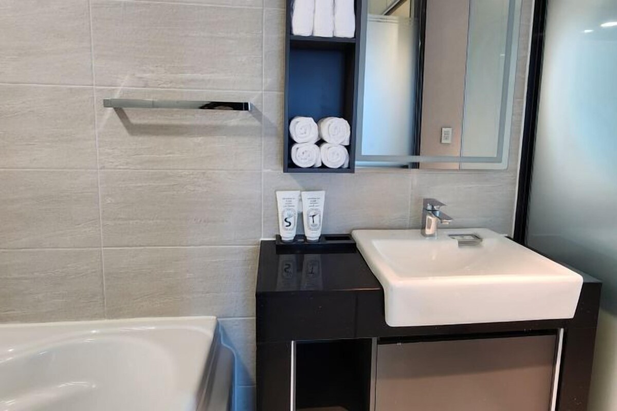 A modern bathroom with a white sink, a mirror, and a shelf with rolled towels.