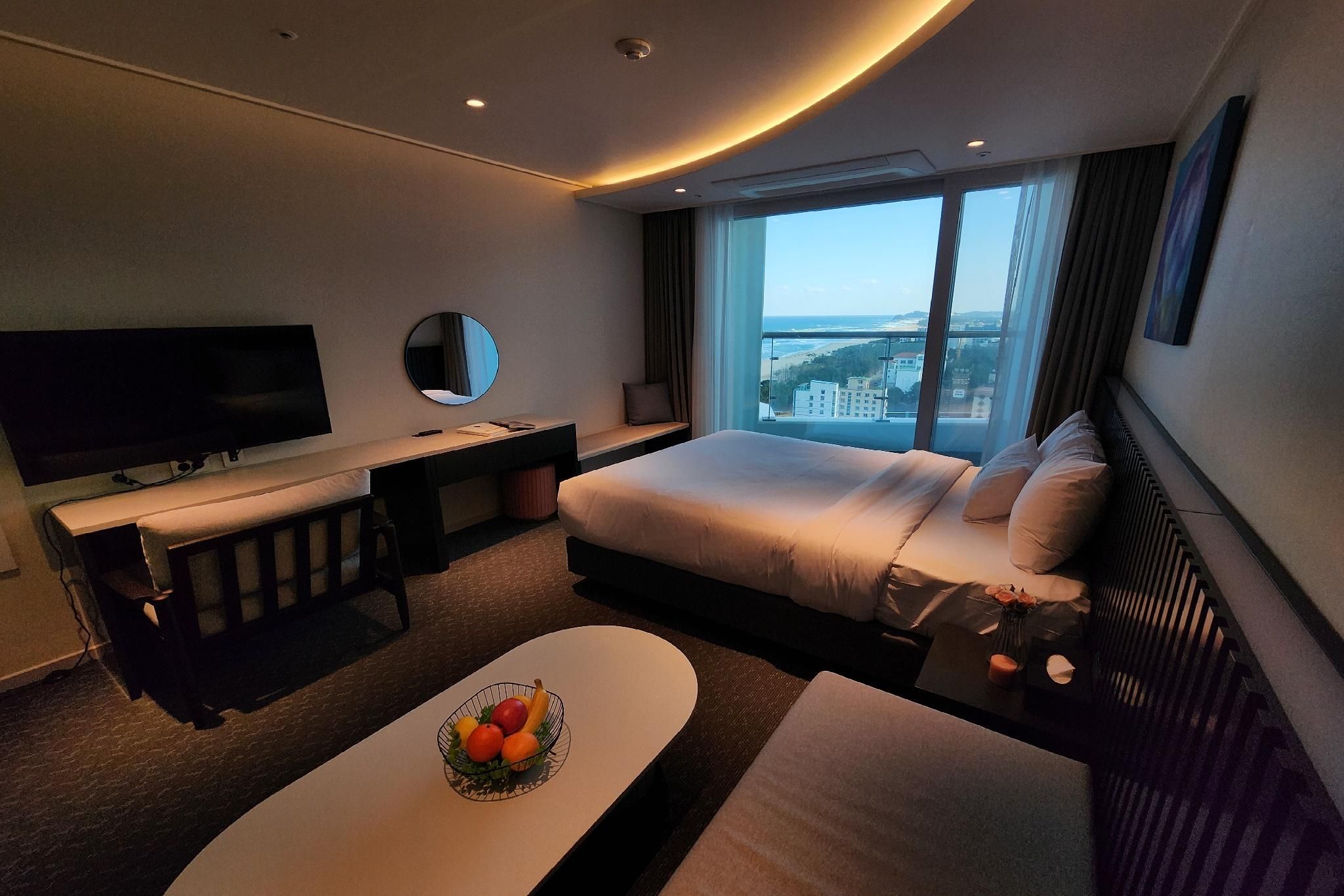 A modern hotel room with a bed, a desk, a TV, and a view of the city.