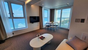 A modern hotel room with a large window offering a view of the ocean, a flat-screen TV mounted on the wall, a round coffee table with a vase and book, and a sofa with a cushion. - Sota Suite Yangyang Granbay (Yangyang)