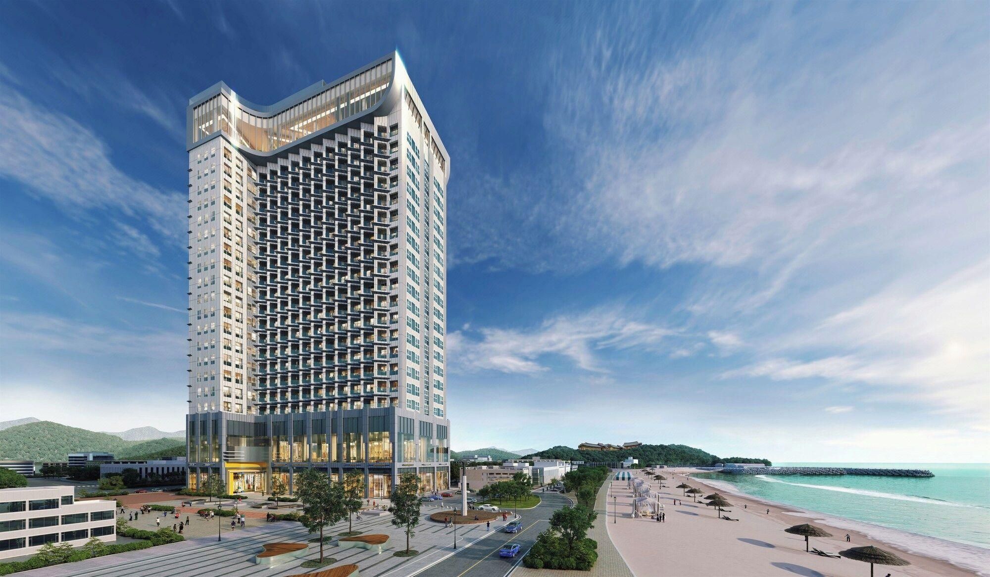 A modern high-rise hotel with a unique facade, situated by a beach with a promenade and a pier.