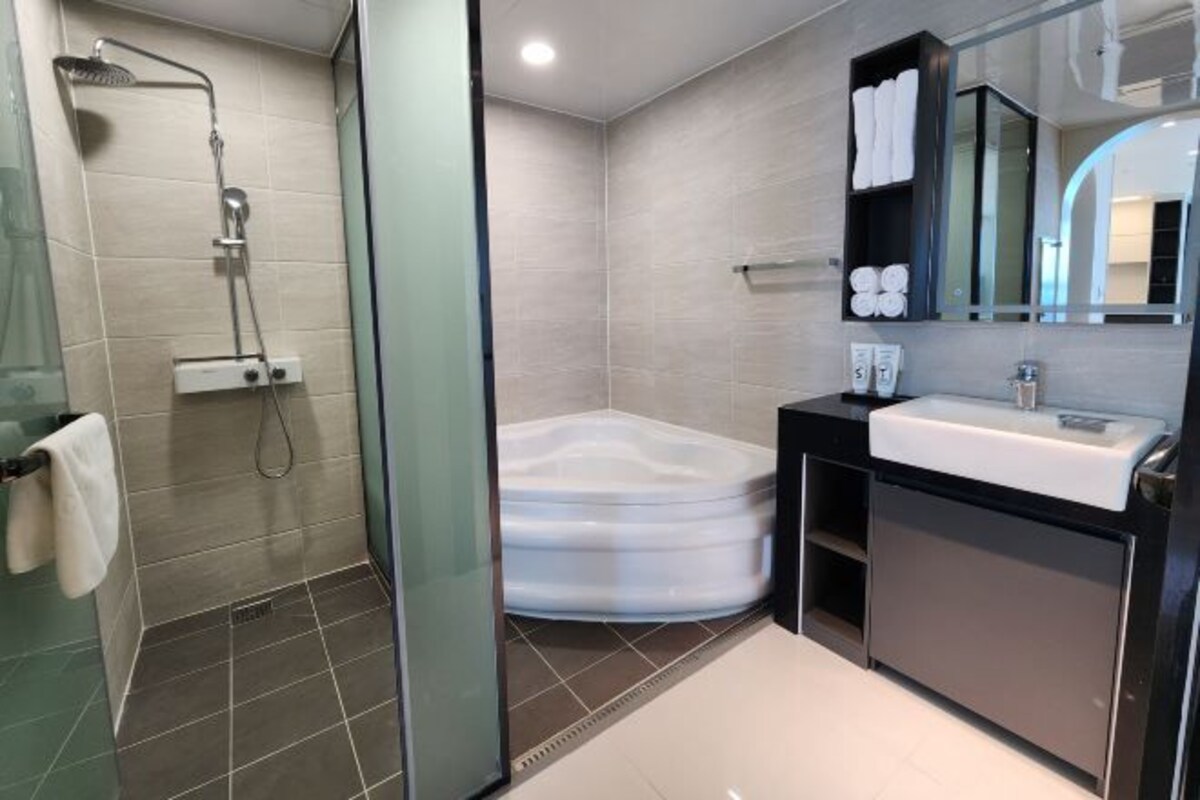 A modern bathroom with a glass shower enclosure, a white bathtub, and a vanity with a mirror.