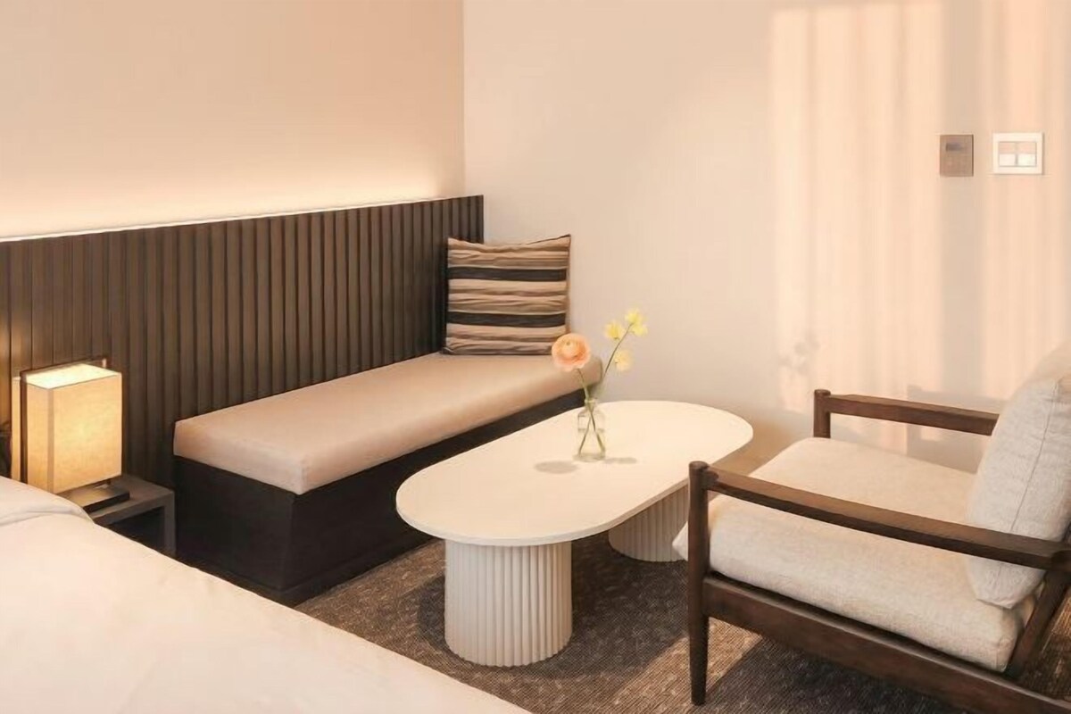 Een moderne hotelkamer met een bank, een tafeltje, een stoel en een bedlamp.