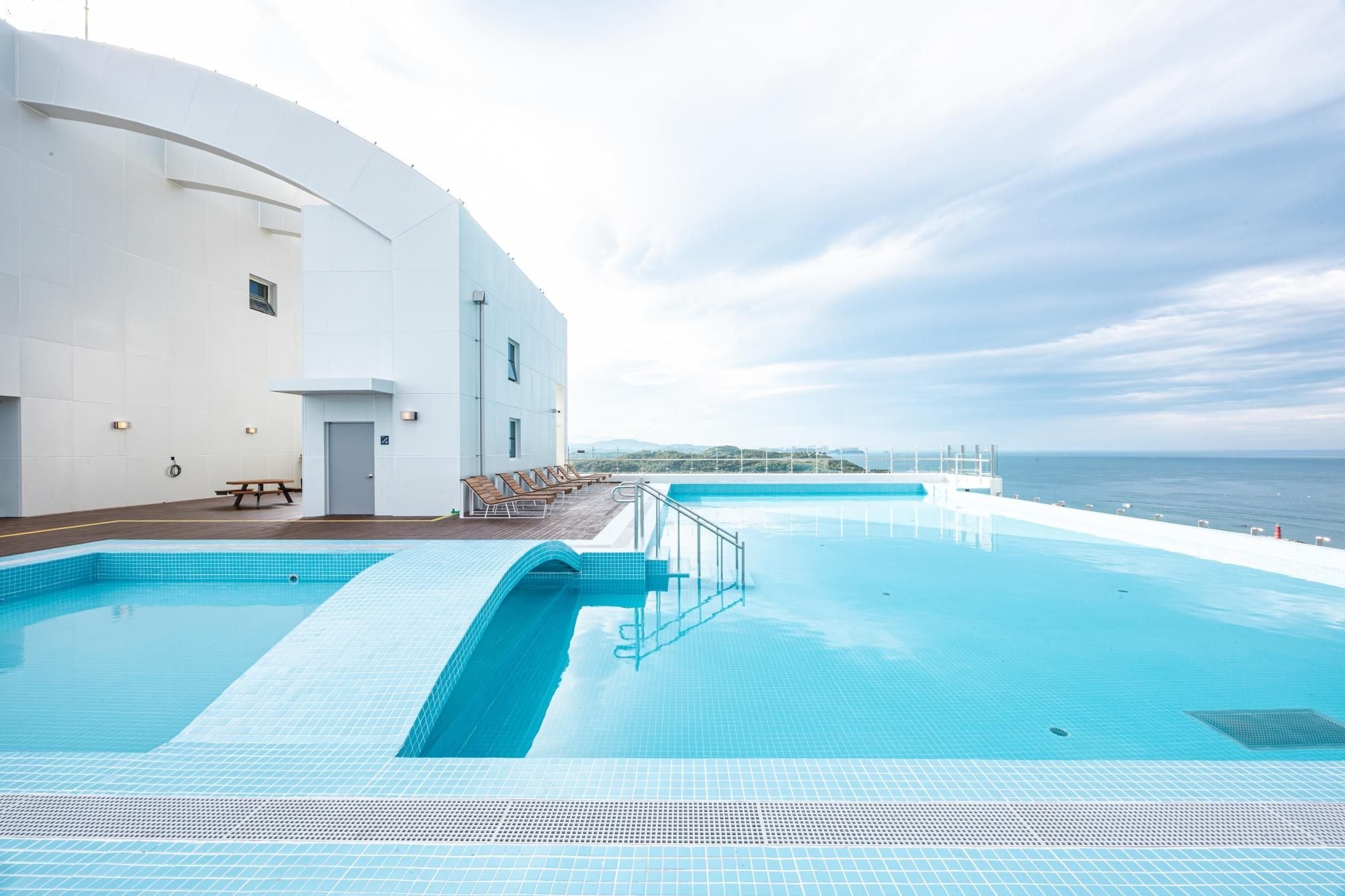 Une piscine avec vue sur la mer, un bâtiment blanc et des chaises longues.