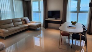 A modern living room with a sofa, a dining table with chairs, a flat-screen TV, and large windows offering a view of the sea. - Sota Suite Yangyang Granbay (Yangyang)