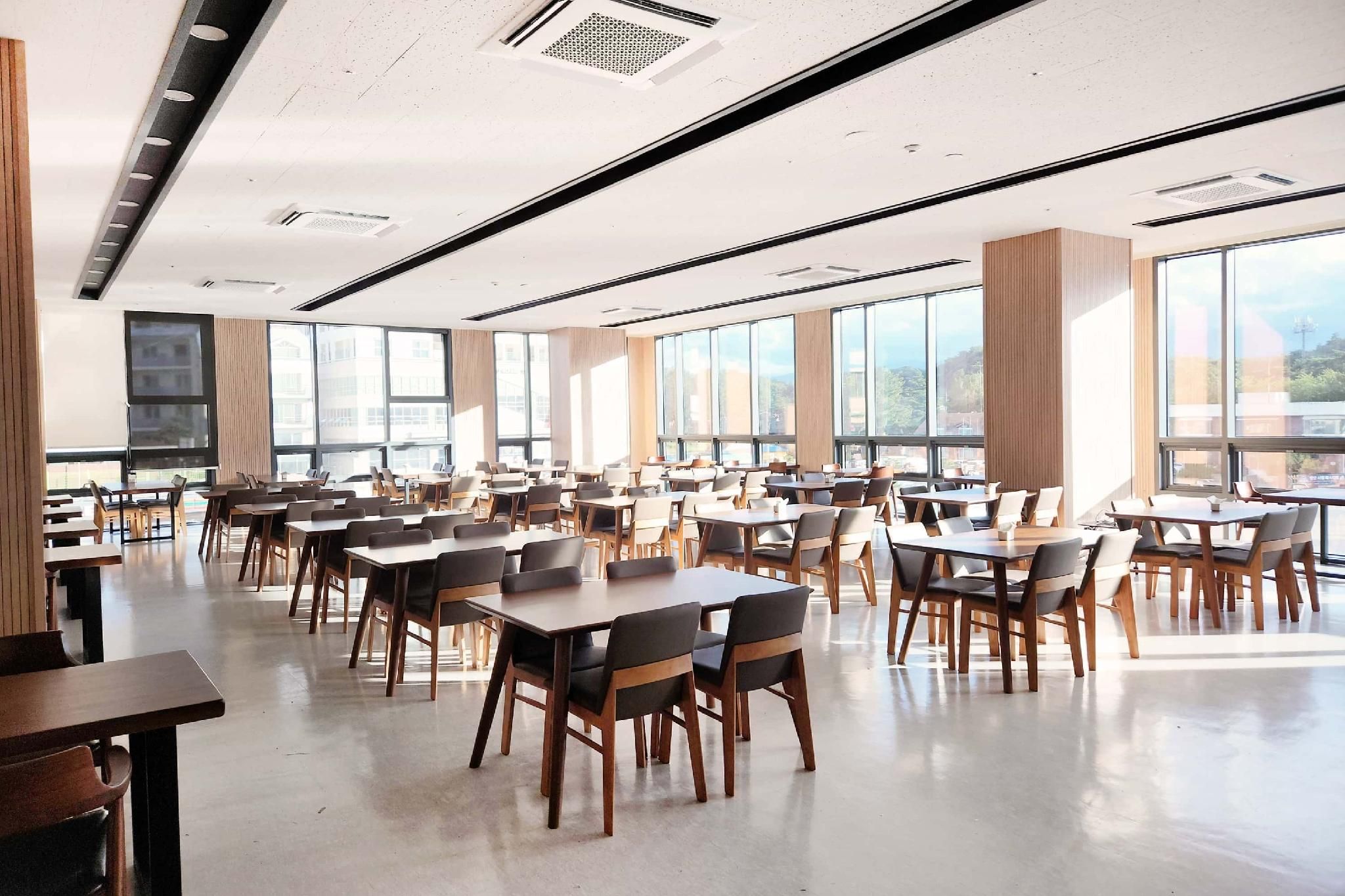 A spacious dining area with multiple tables and chairs, large windows allowing natural light, and a modern ceiling design.