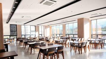 A spacious dining area with multiple tables and chairs, large windows allowing natural light, and a modern ceiling design.