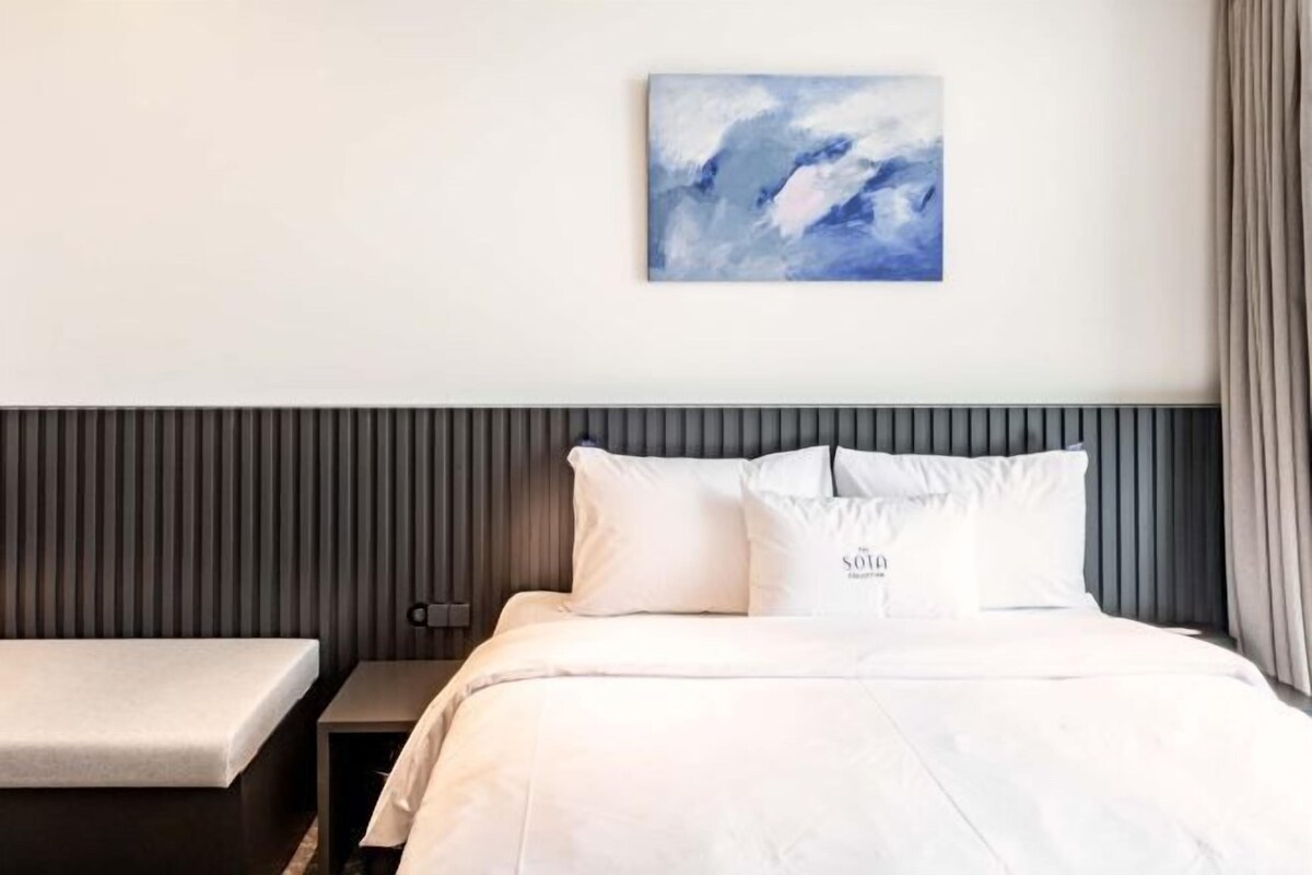 A modern hotel room with a bed, bedside table, and a painting on the wall.
