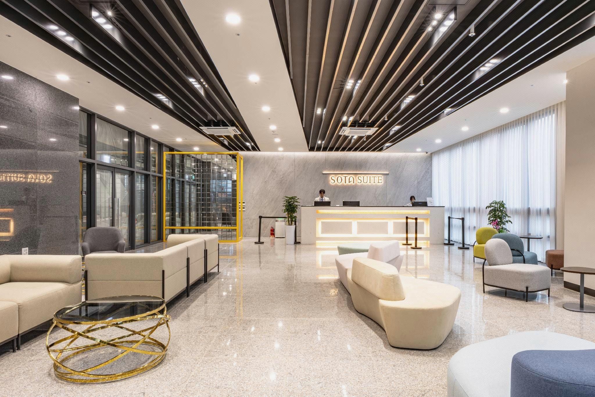 A modern hotel lobby with a reception desk, seating areas, and a glass partition.