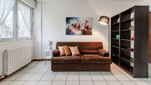Un salon avec un canapé marron, une petite table d’appoint blanche, une bibliothèque et un tableau accroché au mur.