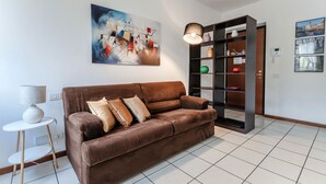 Un salon moderne avec un canapé en cuir marron, une table d’appoint avec une lampe, une bibliothèque et des œuvres d’art abstraites accrochées au mur.