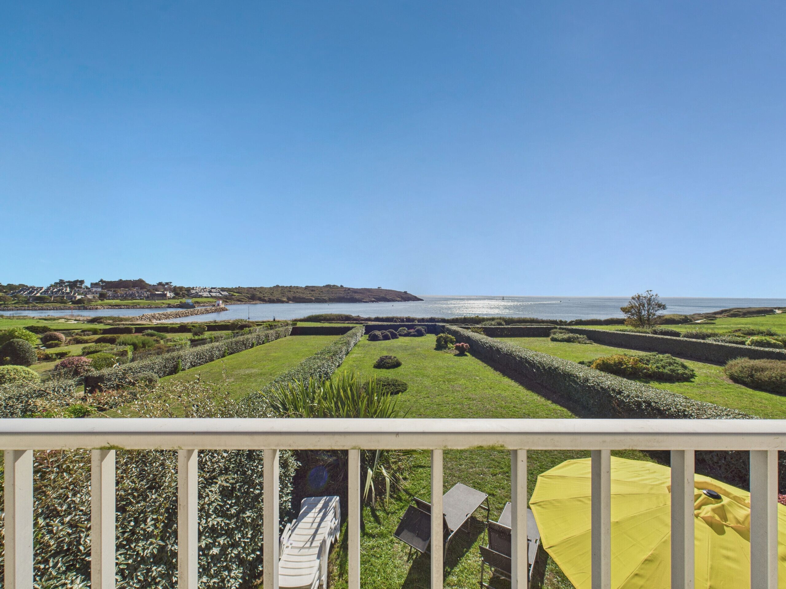 A balcony with a view of a landscaped garden, a body of water, and a distant shoreline.