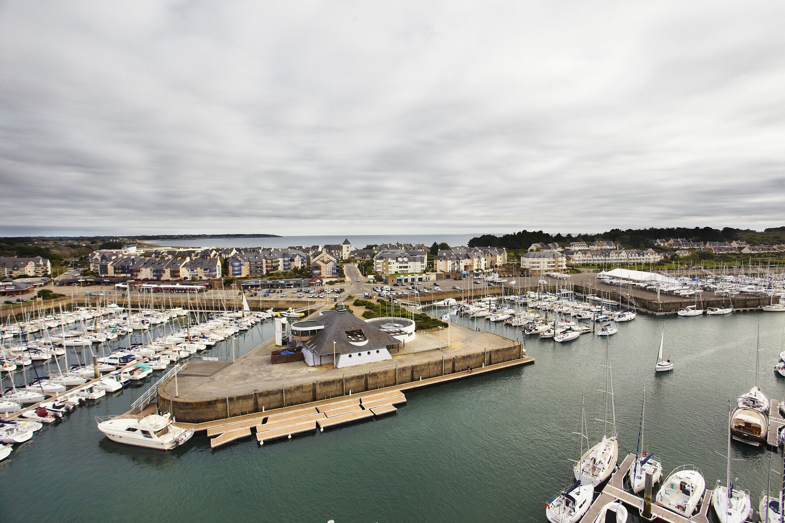 A marina with numerous boats docked, a central building, and a surrounding residential area.