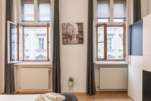 A bedroom with a bed, two windows with curtains, a radiator, and a wall-mounted artwork. - Comfort 3BR Apt Near Wiener Stadthalle (Vienna)