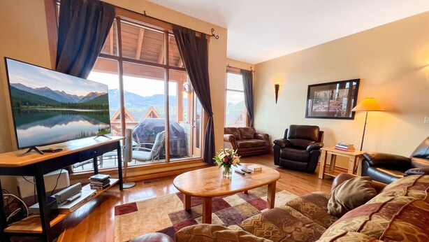 Una sala de estar con un televisor grande, sofás de cuero, una mesa de centro de madera y vistas a montañas a través de amplios ventanales.