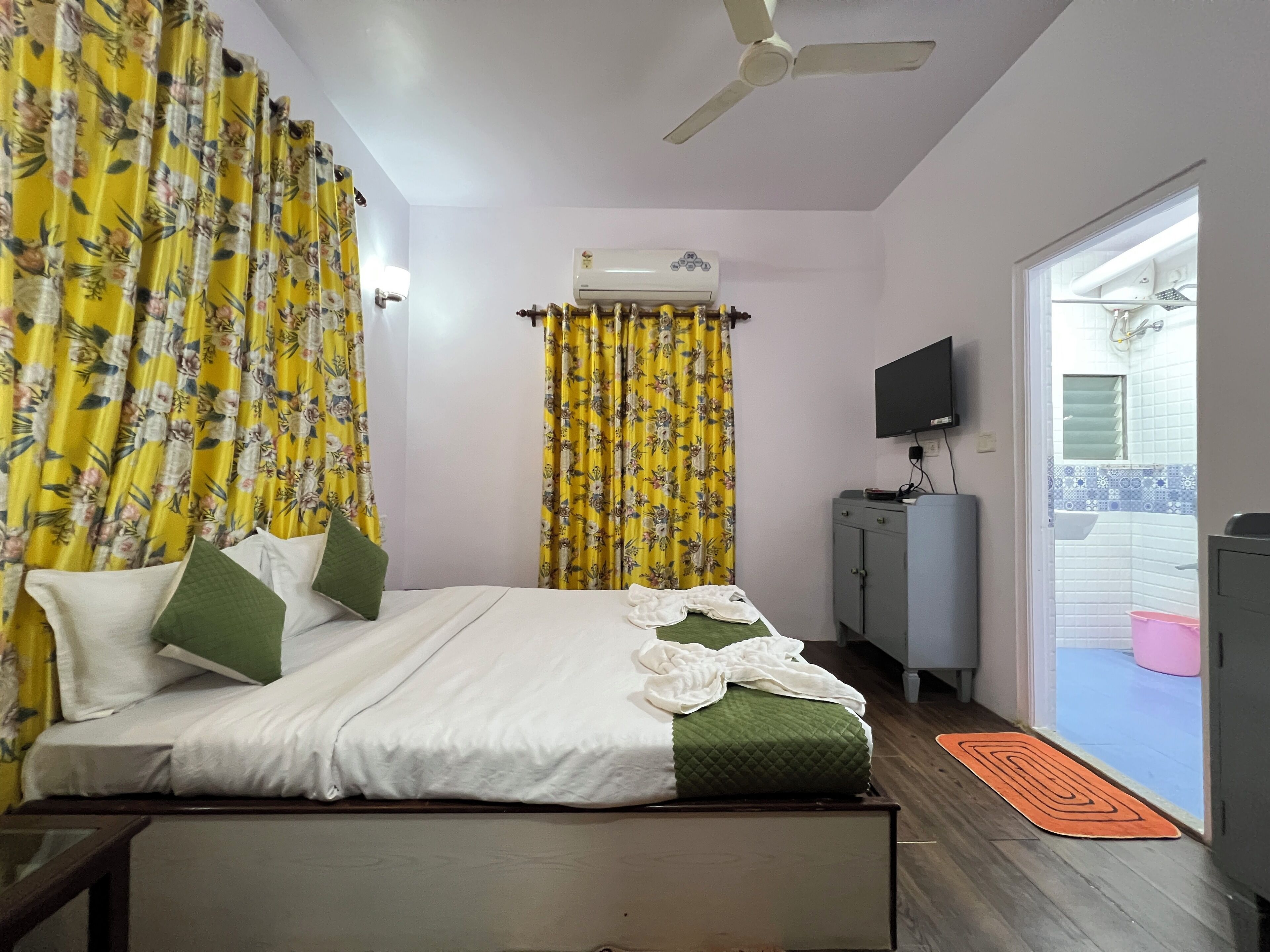 A bedroom with a bed, curtains, an air conditioning unit, a television, and a view of the outside balcony.
