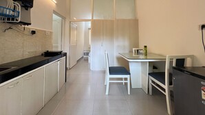 A compact kitchen with a black countertop, white cabinets, a small dining table, and a chair. - Gaur Opulent Goa (Candolim)