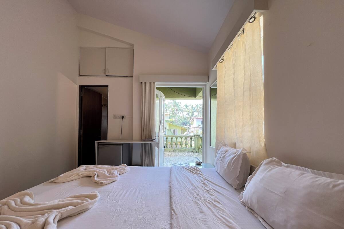 A hotel room with a large bed, a desk, and a view of a balcony with a railing.