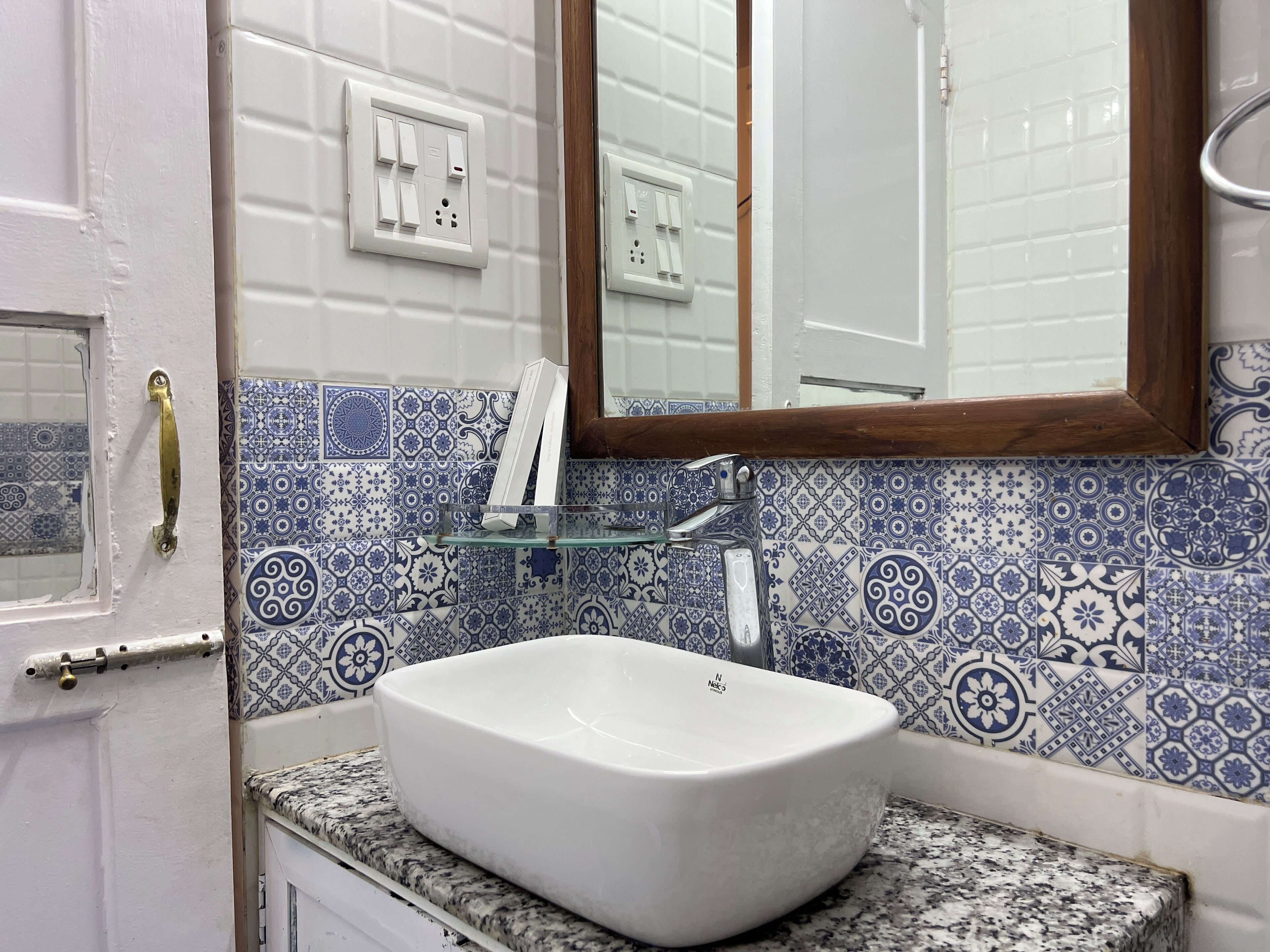 A bathroom with a white sink, blue and white patterned tiles, a glass shelf, and a wooden-framed mirror.